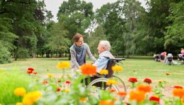 Caregiver and senior man on a wheelchair, walking in park